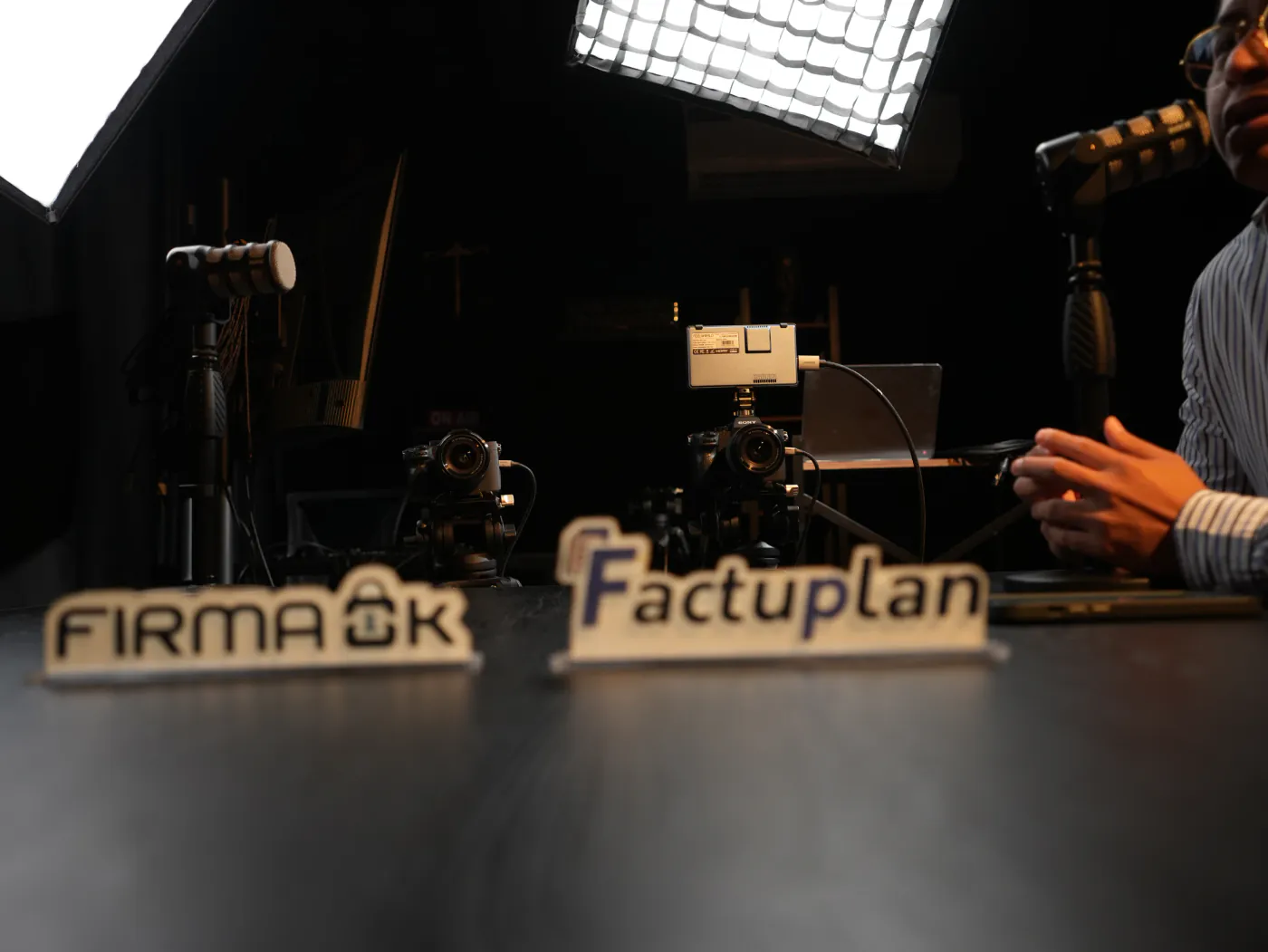 Set de grabación de La Jungla con cámaras, luces y los rótulos de FirmaOK y Factuplan sobre la mesa